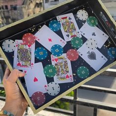 a person holding up playing cards in front of a window with cityscape behind them