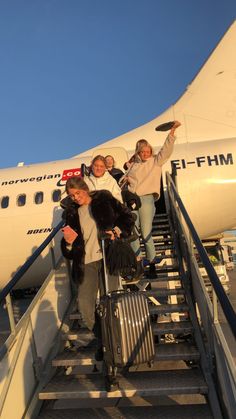 three women are walking up the stairs to board an air plane with their luggage bags