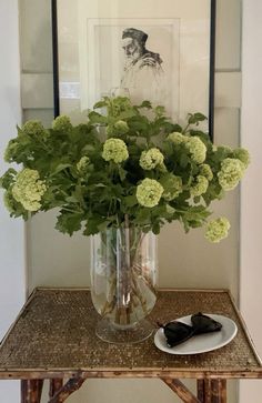 a vase filled with green flowers sitting on top of a table next to a plate