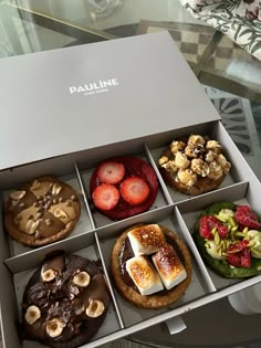 an open box filled with different types of pastries on top of a glass table