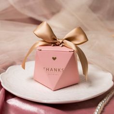 a pink box with a gold bow on top of a white plate and some pearls