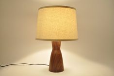 a wooden table lamp with a beige shade on the base and a black cord plugged into it