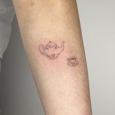 a small teapot and cup tattoo on the left arm by an unknown person's leg