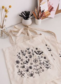 two totes bags sitting on top of a table next to pencils and markers