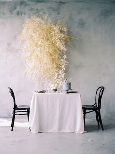 a table with two chairs and a white table cloth on it, next to a plant