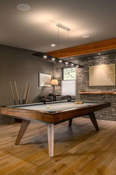 a pool table in the middle of a room with wood flooring and brick wall