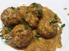 meatballs covered in gravy and garnished with parsley on a white plate