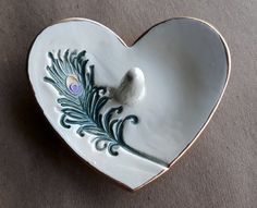 a decorative heart shaped dish with a bird on it's tail and feathers in the center