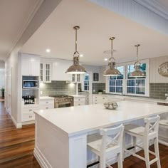 a large kitchen with white cabinets and an island in the middle of the room is lit by two pendant lights