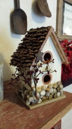 a bird house made out of pine cones and rocks on top of a wooden table