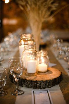 candles are lit in mason jars on a wooden slice at the center of a table