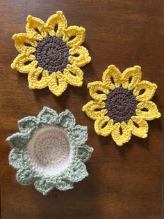 three crocheted sunflowers sitting on top of a wooden table next to each other