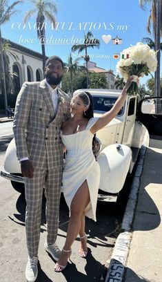 a man and woman are standing in front of a white car with flowers on it