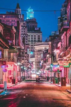 an empty city street at night with buildings lit up in pink and green lights on both sides