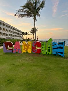 the word beach spelled out in multicolored letters on grass next to palm trees