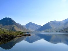 the mountains are reflected in the still water on the lake's edge, while the sky is blue and clear