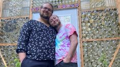 two people standing next to each other in front of a door made out of wine bottles