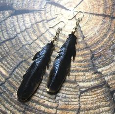 two black feathers are hanging from earrings on a piece of wood