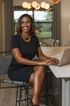 a woman in a black dress sitting at a table with a laptop on her lap