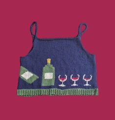 a blue knitted apron with wine glasses and bottles on the front, against a pink background