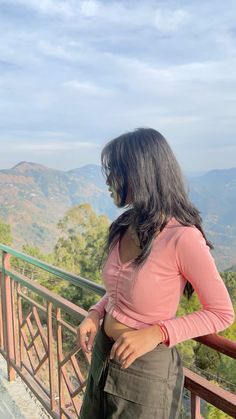 a woman standing on top of a balcony next to a lush green forest covered hillside