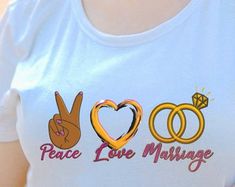 a woman wearing a peace love marriage t - shirt with two rings on her chest