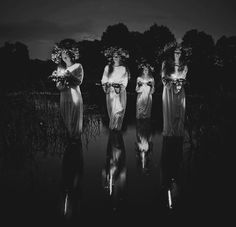 four women standing in the water at night with their hands on their hipss and holding flowers