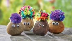 three rocks decorated with fake flowers and googly eyes are sitting on a wooden surface