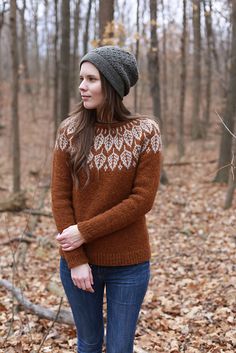 a woman standing in the woods wearing a brown and white sweater