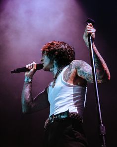 a man with tattoos on his arms and chest holding a microphone in front of him