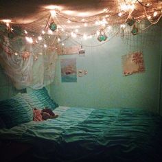 an unmade bed with lights hanging from the ceiling