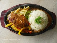 a black plate topped with meat, rice and veggie covered in gravy