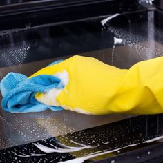 a person in yellow gloves and blue mitt cleaning a black surface with a rag