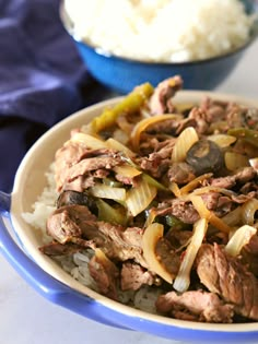 a blue bowl filled with meat and onions on top of rice next to a spoon