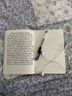 an open notebook with earbuds and headphones laying on a bed next to a quilt