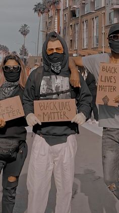 some people holding signs and wearing masks on their faces while standing in the middle of a street