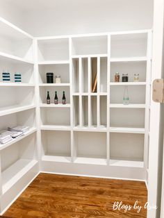 an empty room with white shelves filled with bottles and other items on wooden flooring