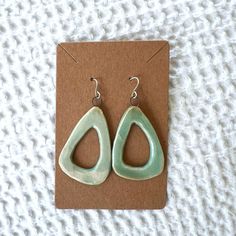 a pair of green earrings sitting on top of a piece of brown paper next to a card