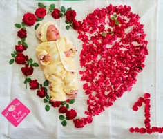 a baby is laying in the middle of rose petals with a heart shaped sign behind it