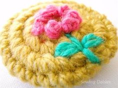 a crocheted brooch with pink and green flowers sitting on top of it