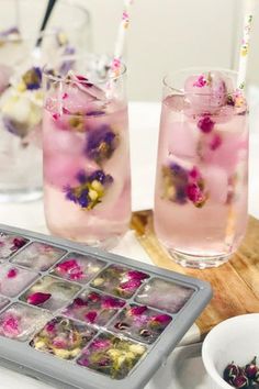 three glasses filled with ice and flowers on top of a wooden tray next to bowls