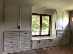 an empty room with white cabinets and drawers on the wall, next to a window