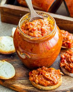 a jar filled with sauce sitting on top of a wooden cutting board next to bread