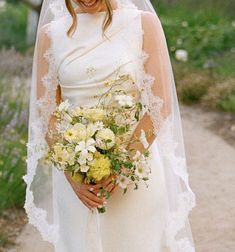 a woman in a white wedding gown holding a bouquet of flowers and smiling at the camera