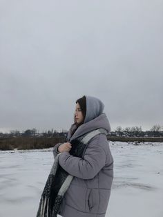 a woman standing in the snow wearing a gray coat and scarf with her hands on her hips