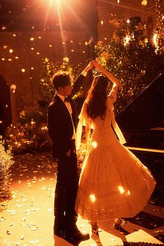 a man and woman standing next to each other in front of a piano with lights on it