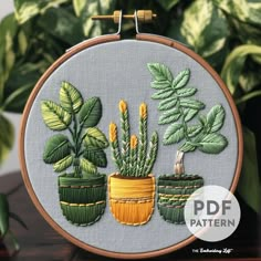 the embroidery pattern shows three potted plants with green leaves on them, in front of a planter