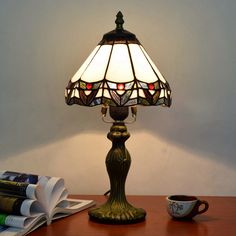 a lamp sitting on top of a wooden table next to a cup and bookcase