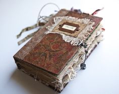 an old book is covered with torn paper and lace, sitting on a white surface