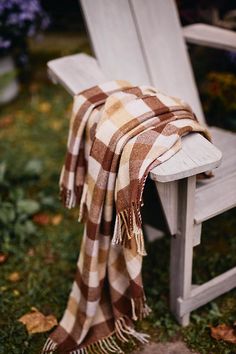 a plaid blanket draped over an old wooden chair on the grass in front of flowers